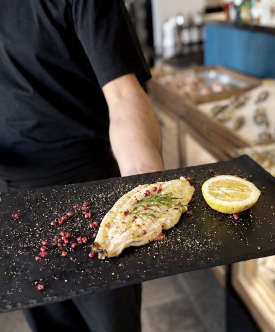 A fillet of the day's catch on black slate with pink peppercorns and charred lemon