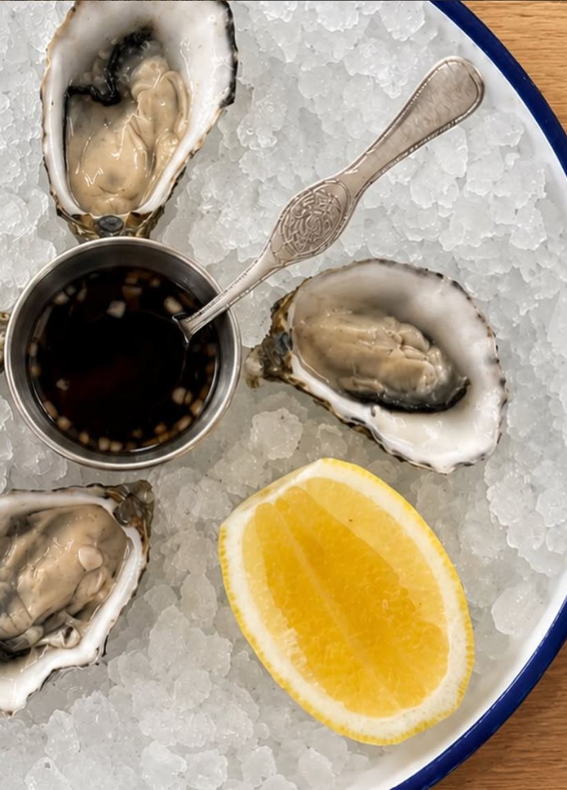 Oysters on crushed ice with ponzu mignonette and lemon, on an enamel plate