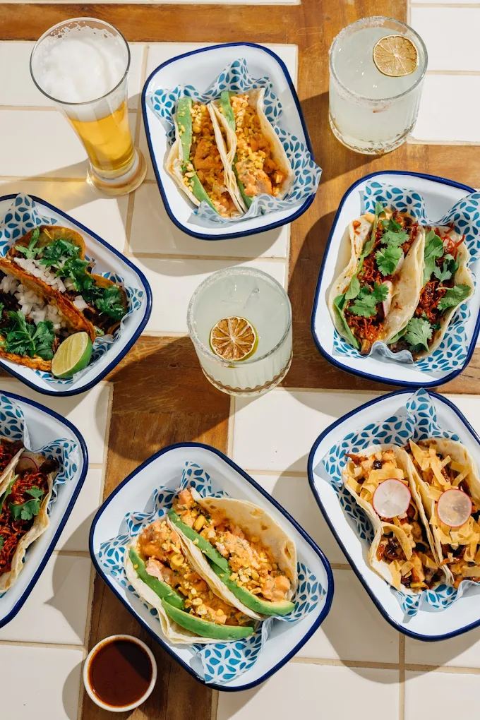 Enamel trays of assorted tacos with margaritas on a tiled table